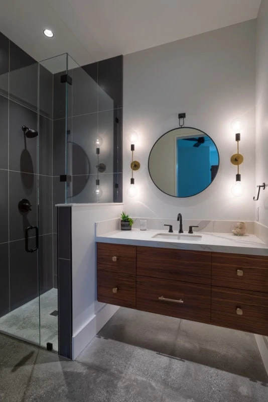 Single vanity floating sink with circle mirror and black walk in shower