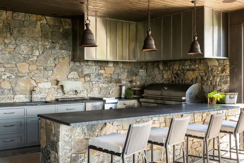 covered outdoor kitchen built into stone wall with bar top and counter height stools
