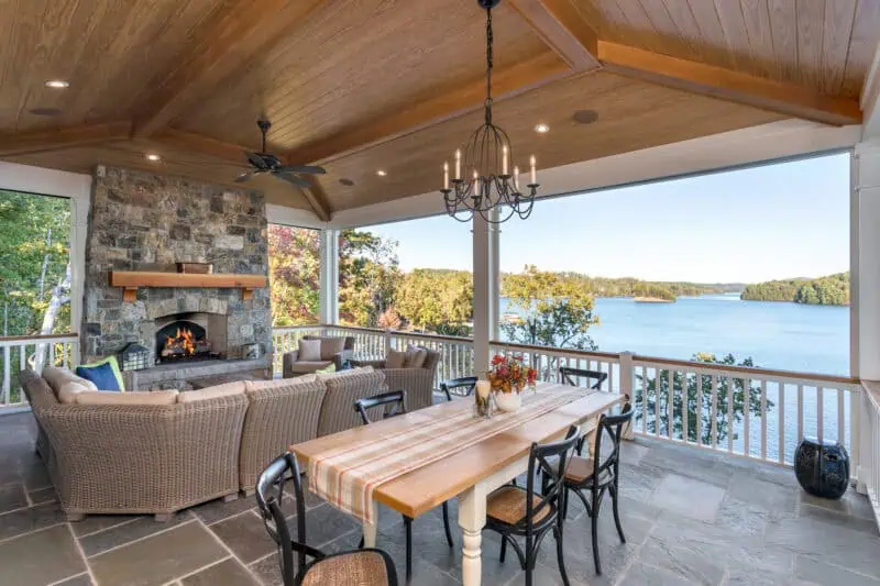 covered outdoor living area overlooking a lake with dining table and sectional in front of a fireplace