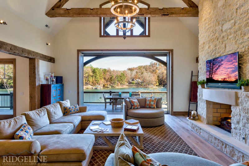 living room with light brown couches, blue & orange accent pillows, tan stone fireplace and open window overlooking lake keowee