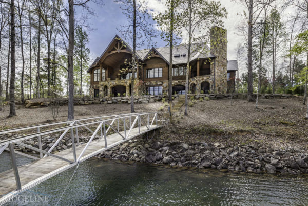 back of large brown lake house with bridge going out to dock on lake