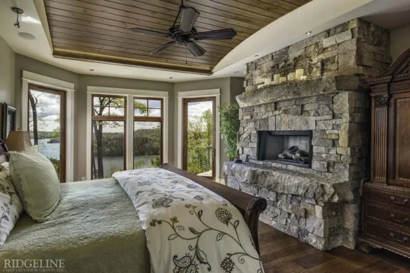 master bedroom with massive stone fireplace and large windows overlooking lake