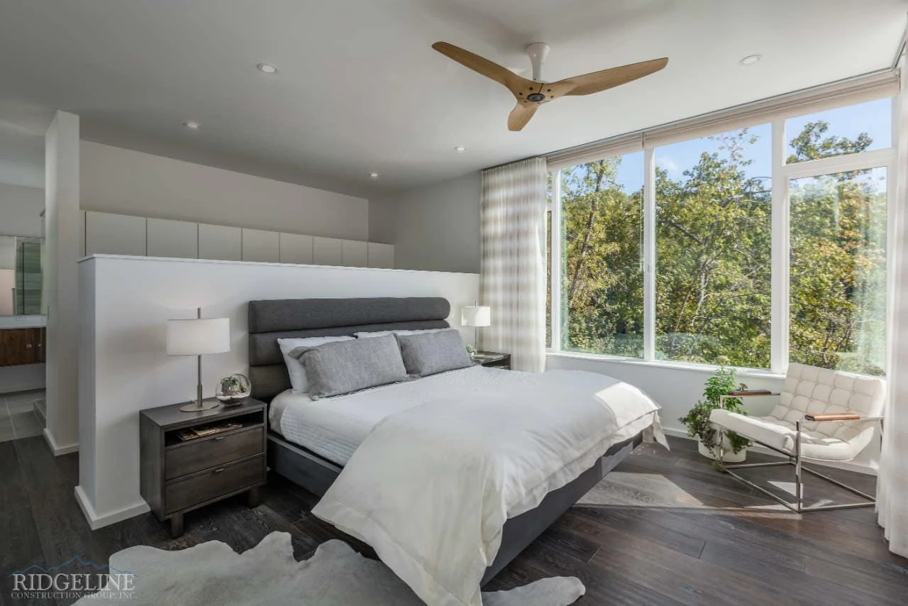 master bedroom with white comforter and large windows overlooking trees