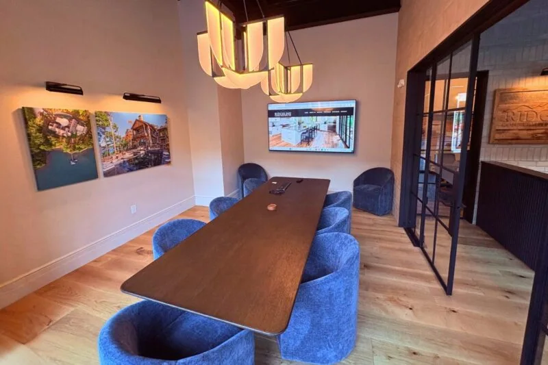 Modern conference room with wooden table and blue chairs, wall art, and a large screen.