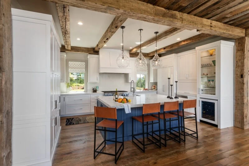 blue island with bar height chairs in a white modern kitchen with rustic wooden ceiling beams