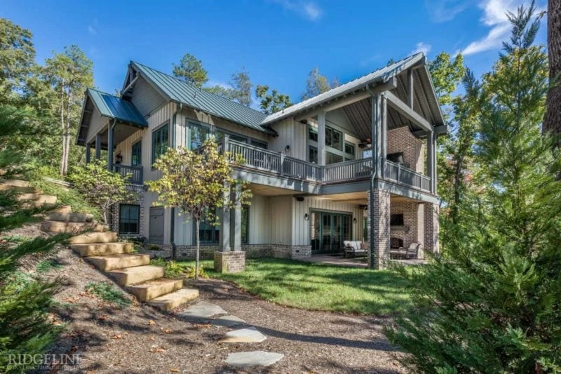 The outside of a beautiful home, surrounded by nature, with an outdoor balcony and sun panel roofing