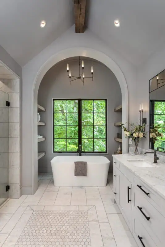 Ridgeline Design Studio of a master bathroom with arched doorways, stand alone tub in front of a window and detailed tiled flooring.